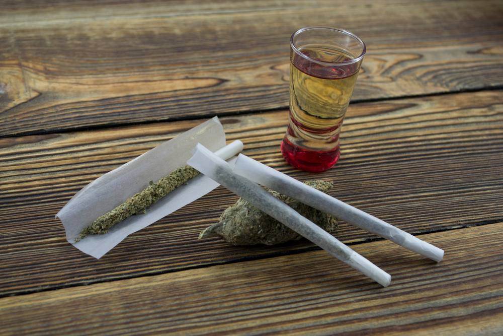 Joint, grinder, cannabis buds, alcohol shot and related items on a table