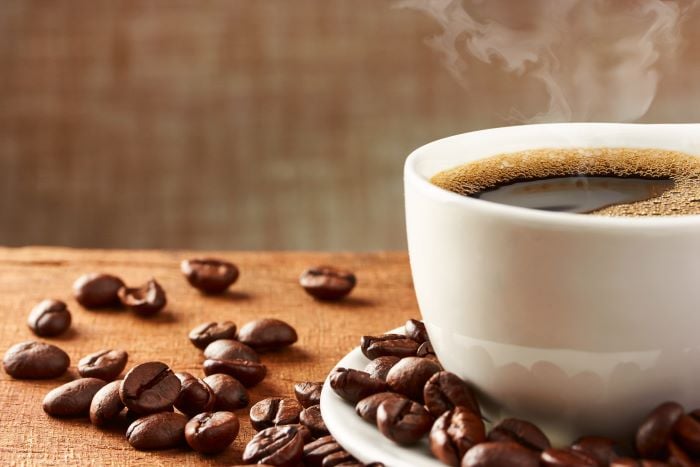 cup of coffee on a wooden table with coffee beans scattered around it