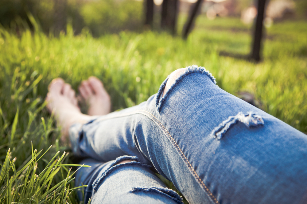 legs of hipster woman wearing torn jeans lying in green grass