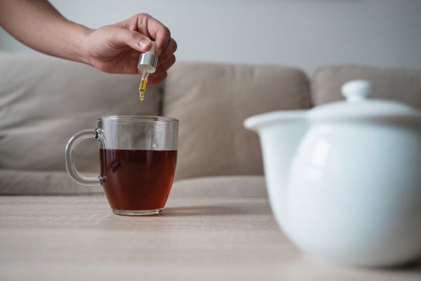 woman eye dropping cannabis oil in hot tea