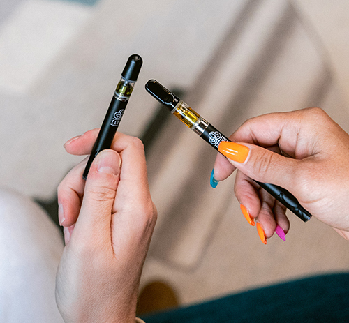 two people holding marijuana vape pens